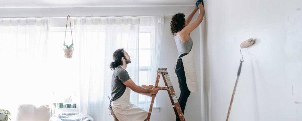 A man and woman work on painting a room.