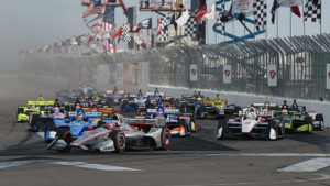Secondly, the stands with the crowd are featured in this photo. The multi colored cars are on the track in front of the fence parked.