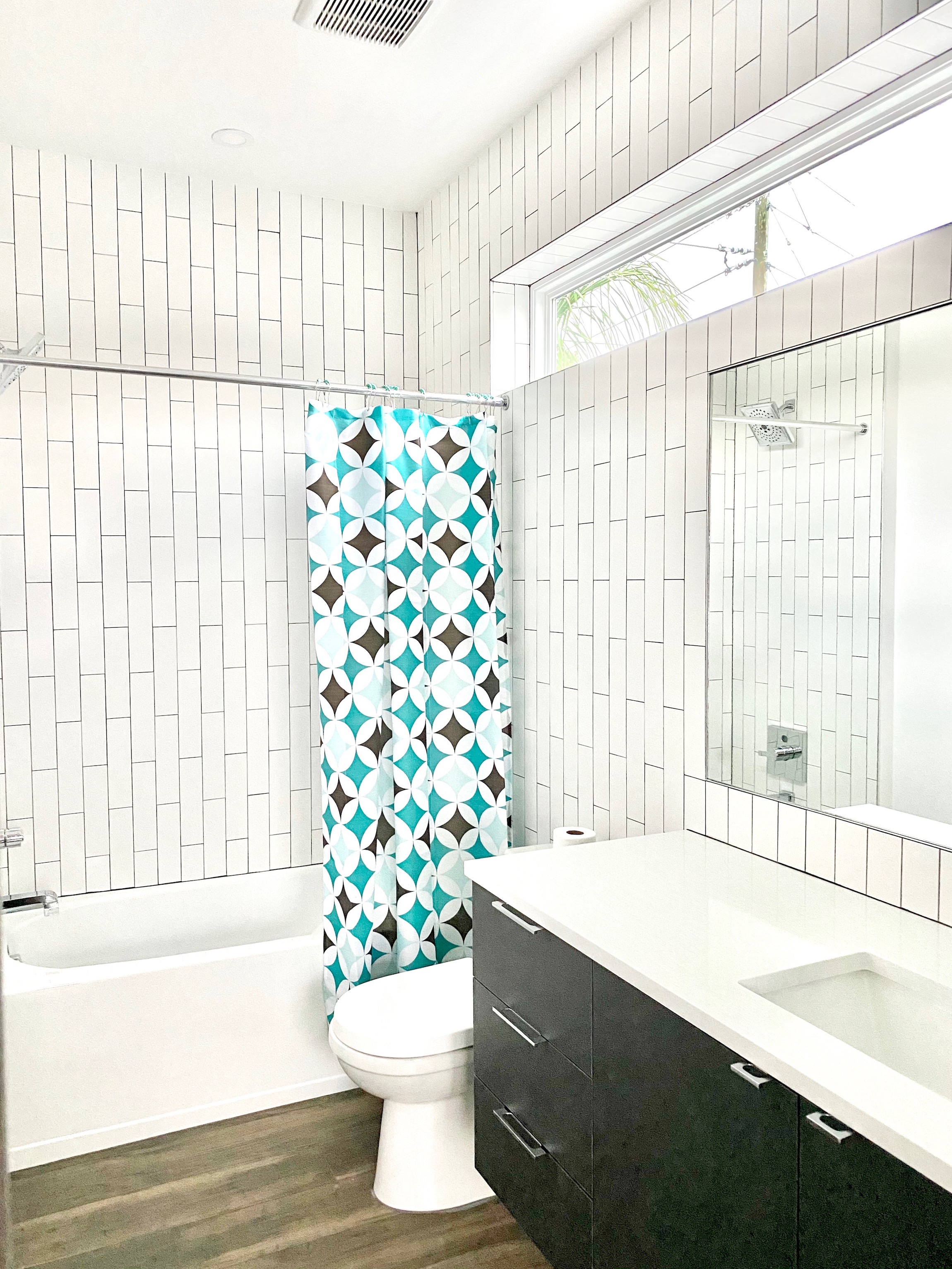 Also, A large window extends across the top wall of the bathroom of the Kasper Modern Home. And the tile is a white matte color, and the vanity is a black stained wood.
