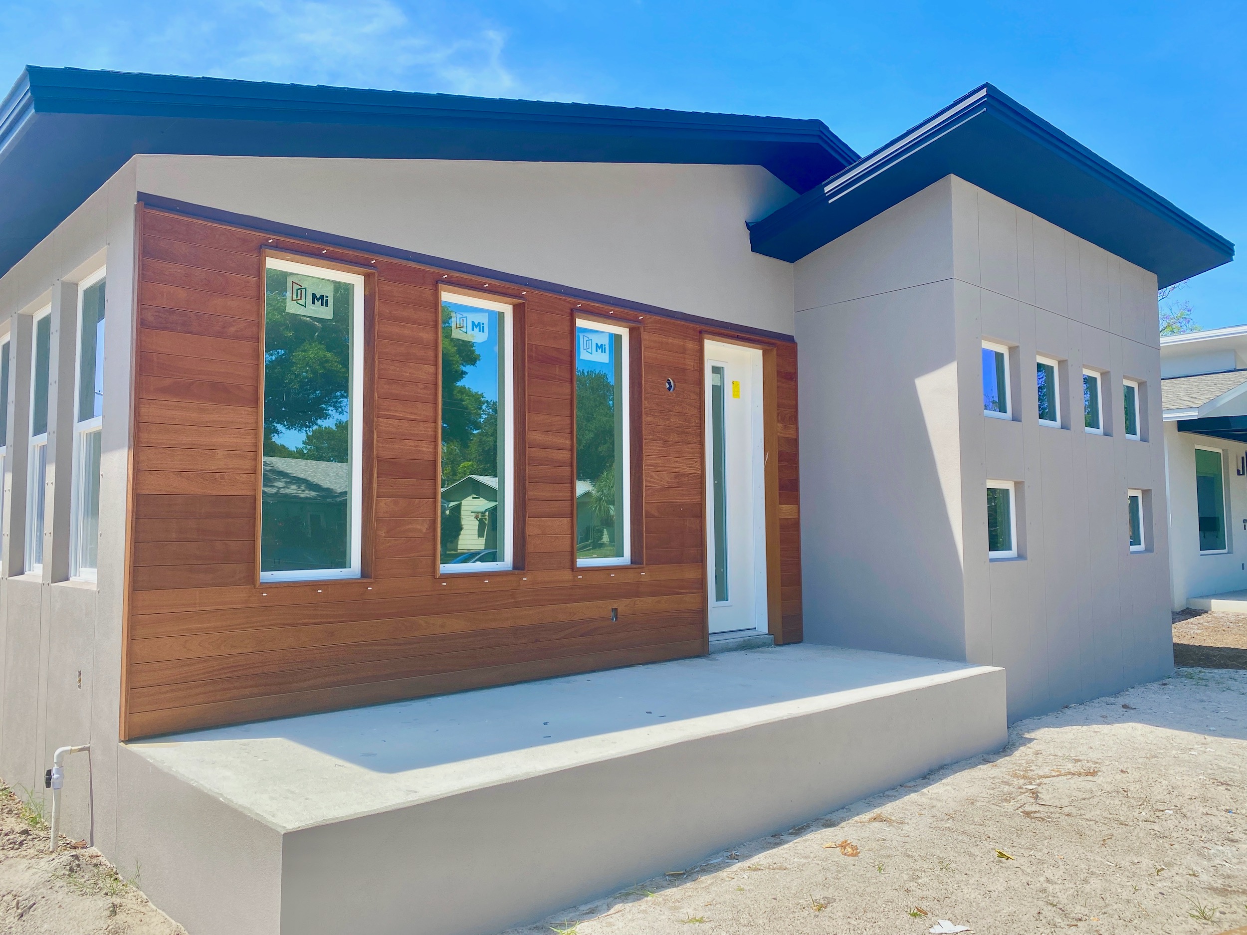 Additionally,Currently Under Construction, this home is flanked with walls of windows.. And the trim is black and a gray stucco siding. Moreover, there is a wood faced front porch.