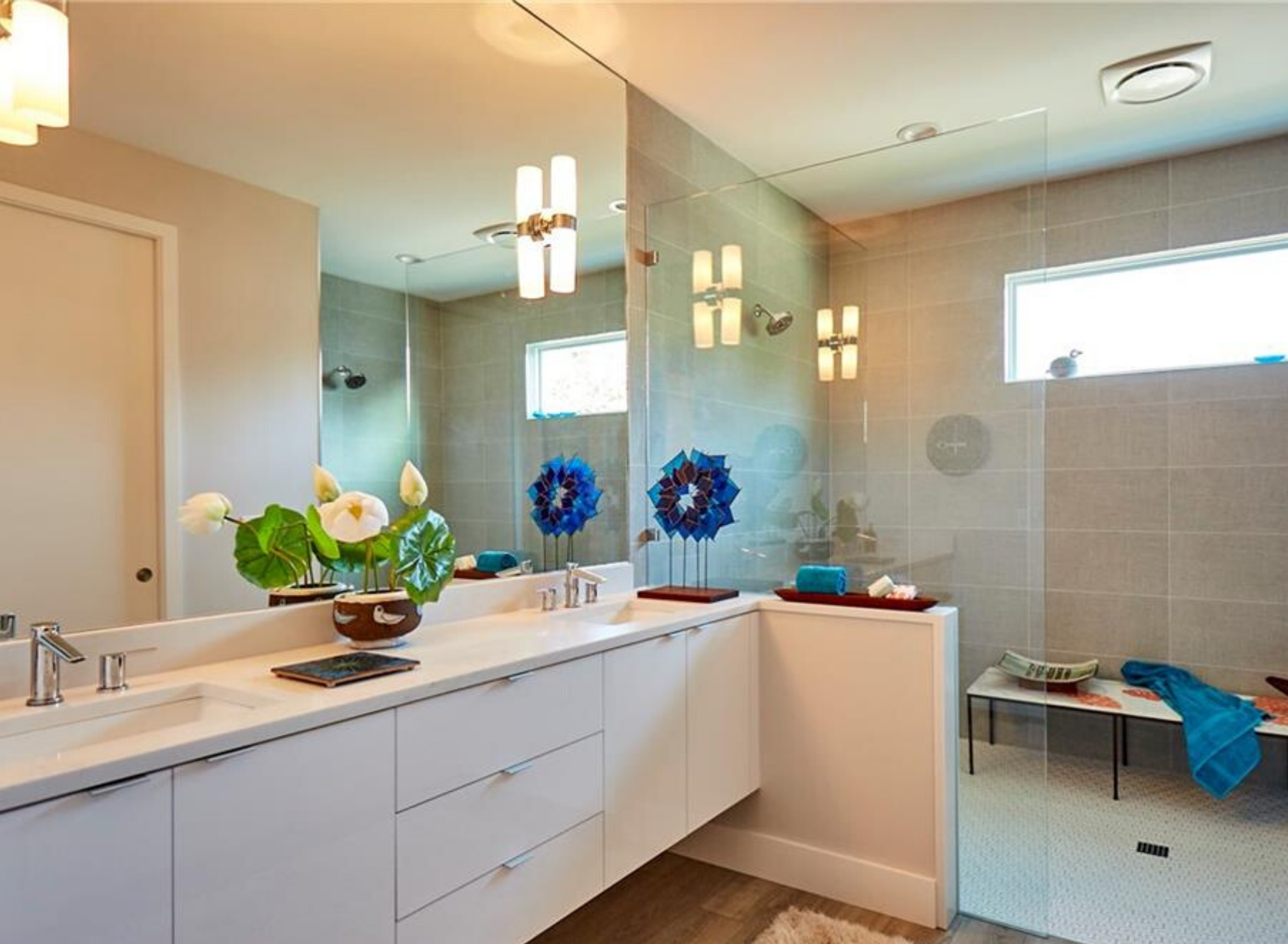 First,The large horizontal window gives blue sky views from the shower. And the full wall vanity mirror reflects the light throughout the bathroom.