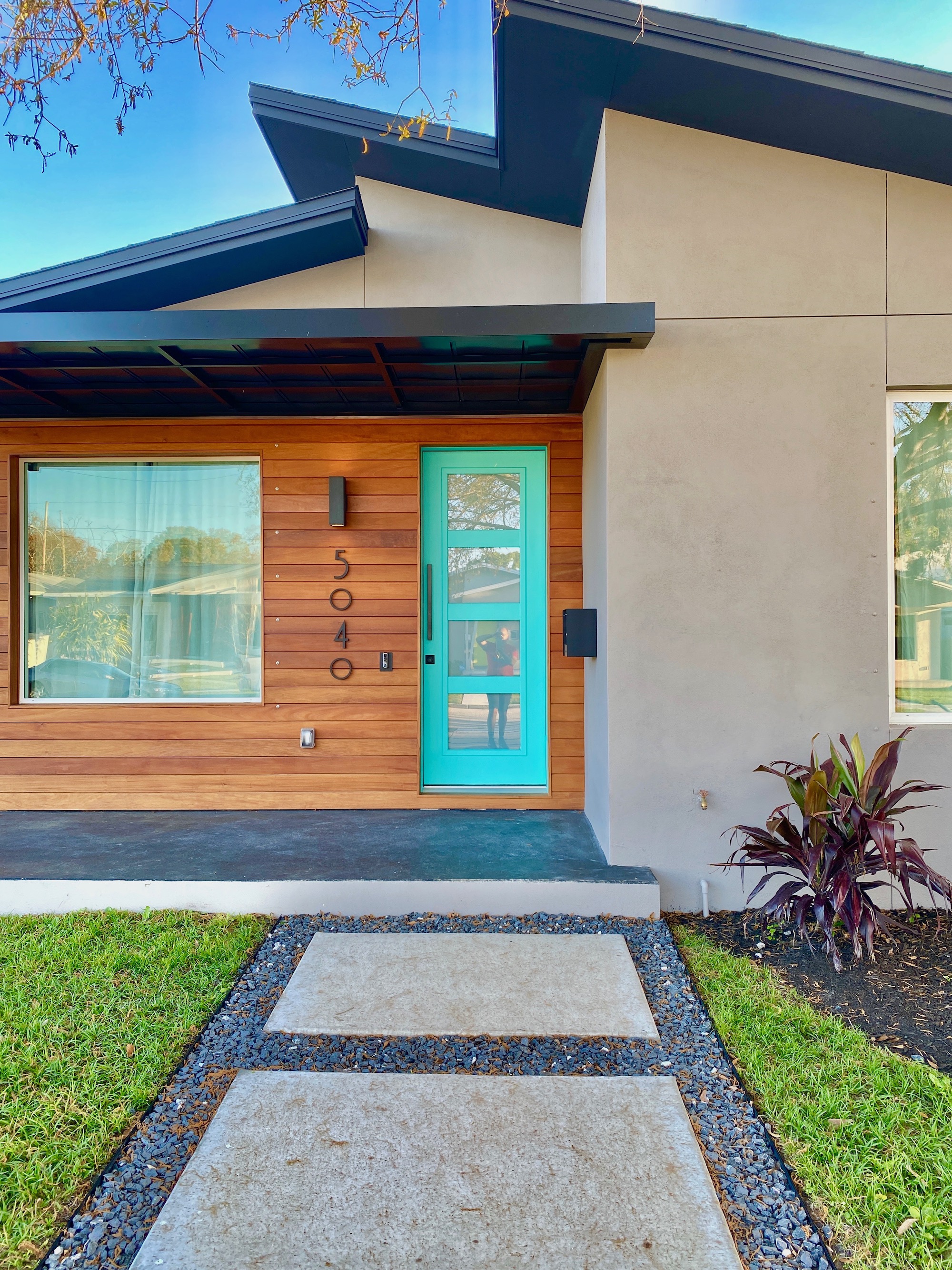 Therefore, A custom Modern Sidewalk and a stained concrete front porch welcome guests. Also, the front door is a tiffany blue color.