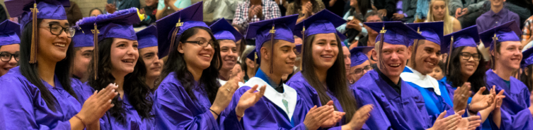 A group of seated students dressed in purple graduation gowns and caps