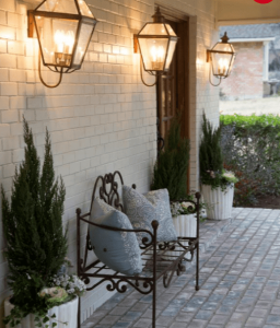Exterior home photo showing a wall with sconces and a paver patio with a wrought-iron bench