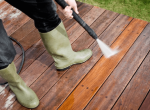 Downward looking view of a person wearing boots and holding a power washer, spraying a wooden deck