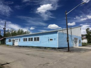 Light blue building on a street corner with two garage doors and blue sky in the background