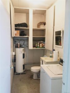 Grungy looking bathroom with commode, sink, mirror, washing machine, and lots of closet space on the wall
