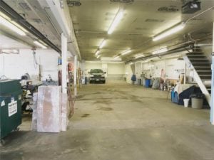 Long interior garage with concrete floors, fluorescent lighting, and equipment along the walls
