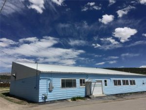 Angled view of a blue building with white roof, garage bay, and several windows