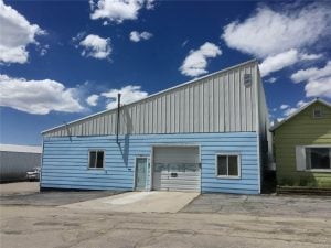 Side view of blue and white building with sloping roof, garage bay, and two windows