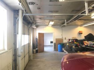 Photo looking at an open door leading into an empty room; foreground shows part of a dark red vehicle and a couple snowmobiles
