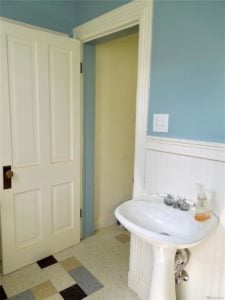 White sink and wainscoting in a bathroom with teal wall paint and a white door