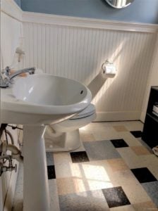 White, dark blue, light blue, and tan floortiles in a bathroom showing white commode and sink