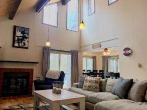 Room with high vaulted ceiling, clerestory windows, fireplace, and large sofa; kitchen is visible in the background