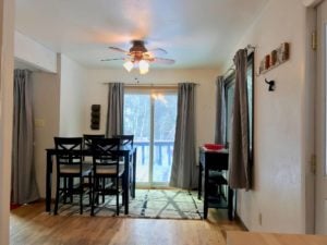 Dining area with high square table and matching chairs; curtains are open showing a sliding glass door to the deck
