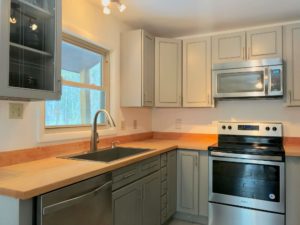 Kitchen view showing the sink, open window, stove, microwave, and some light gray Shaker-style cabinets