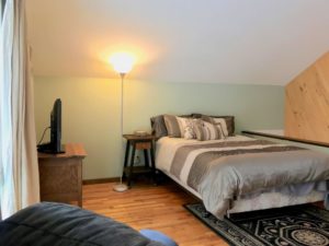 View of bedroom showing full-size bed, nightstand, floor lamp, and small dresser with flatscreen TV