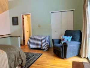 Bedroom with light green walls, black sofa chair, white closet doors, and open bathroom door