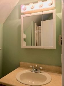 Round white sink and three-door cabinet with four light bulbs at the top