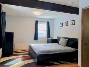 Black bed, dresser, and nightstands in a bedroom with white walls and exposed rafter