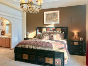 King-size bed in carpeted bedroom with huge chandelier; arched entryway to bathroom is visible on the left