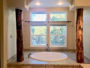 Oval drop-in tub set back into an alcove with two log pillars and a window behind