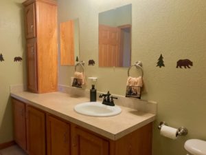 Bathroom vanity with single sink and mirror, tons of cupboards space to the side and underneath. Walls are a light olive green color