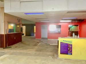 Back area of bowling area where games/concessions used to be, I think. There's a bright yellow service desk with a purple poster, concrete floors, and some bright red walls in the backround