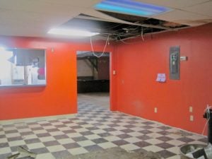 Room with bright red walls and black-and-white checkered floortiles; parts of the ceiling are gone or hanging down. Very classy.